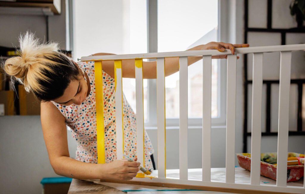 A woman painting a baby crib with a yellow paint
